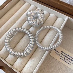 Three silver spiral hair ties in a wooden jewelry box with soft beige lining