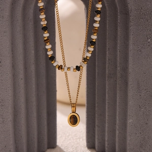 Double-layered beaded necklace with a tiger eye pendant on a grey concrete pedestal