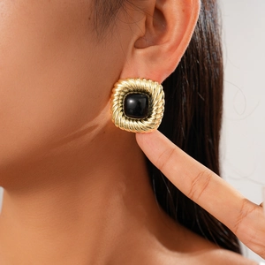 Detail of square gold twist earrings with black gemstone worn on model's ear