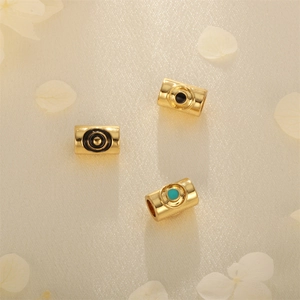 Golden cylindrical evil eye charms for DIY jewelry making on a beige floral background