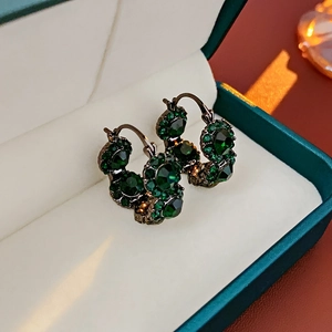 Detailed close-up of emerald crystal cluster earrings with gunmetal finish on jewelry box