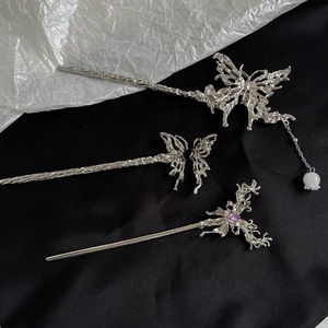 Detailed macro view of three silver liquid metal hair pins with butterfly and gemstone motifs