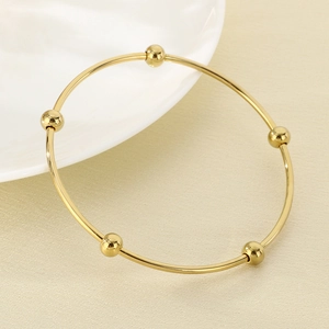 Detailed view of gold stainless steel bangle with five integrated beads on textured fabric