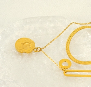 Detail view of double-layer gold chain necklace with heart and ring charms on glass