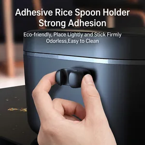 Adhesive rice paddle holder made of black plastic mounted on a rice cooker side