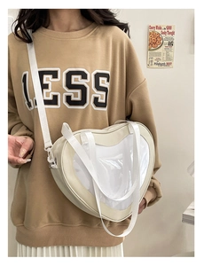 Detail of white heart-shaped ita bag featuring clear window and adjustable shoulder strap