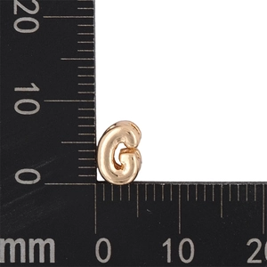 Detail view of a mini golden letter G pendant measured with a ruler for size accuracy