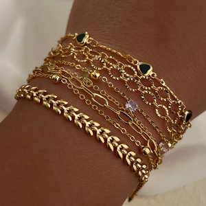 Detail of layered gold bracelets featuring emerald heart charm and wheat link patterns
