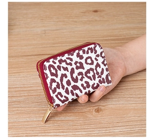 Close-up of leopard print card wallet with gold zipper held in hand over wood desk