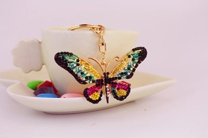 Close-up of a golden butterfly keychain with colorful crystals on a white ceramic saucer