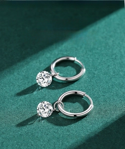 Detailed view of silver hoop earrings featuring brilliant round-cut zircon pendants on green background