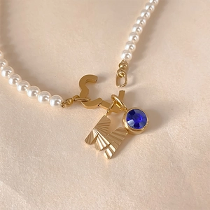 Vue détaillée d'un collier de perles avec lettre M dorée et pendentif cristal bleu