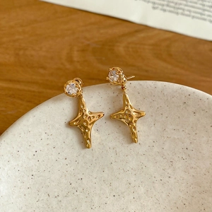 Macro detail of gold plated star drop earrings with zircon on a ceramic dish