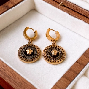 Detailed close-up of golden Medusa head earrings with Greek key patterns on white lining