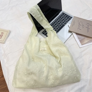 Detail of light green tote bag featuring white floral embroidery and soft fabric texture
