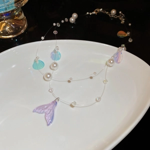 Detailed macro of iridescent mermaid tail pendant and pearls on a ceramic tray