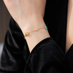 Detail of a gold bracelet with ladybug charm, turquoise beads, and a crystal clover