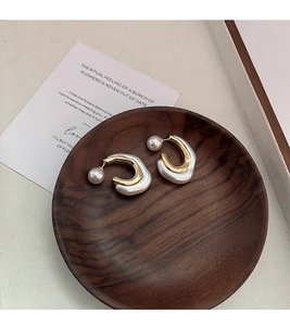 Detail view of retro C-shaped pearl stud earrings on a dark wood tray display