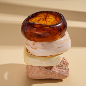 Three-piece geometric resin bangles in amber, marble white and yellow on stone display