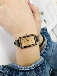Close-up of a stylish women's rectangular watch with rose gold case and brown leather strap