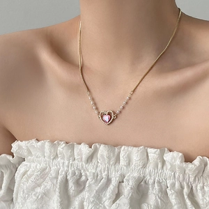 Elegante collana a cuore dorata con gemma rosa e piccole perle su una modella