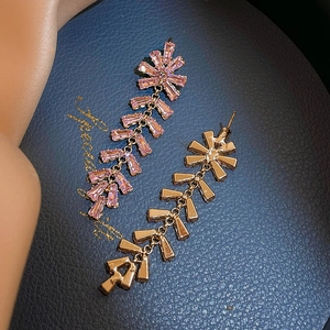 Elegant rose gold drop earrings with pink zircons and tassels on blue leather background