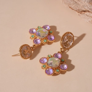 Detail of vintage gold earrings with purple gemstone and portrait cameo on rustic rock