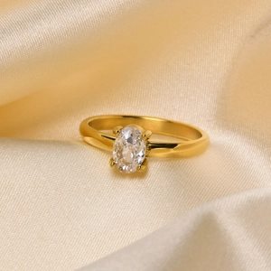 Close-up of golden titanium ring with oval zircon on champagne silk background