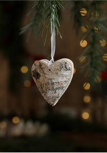 Close-up of heart-shaped wooden Christmas ornament hanging on a pine branch with warm bokeh