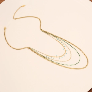 Chic multilayer golden necklace featuring tiny green beads and turquoise charms on a beige base