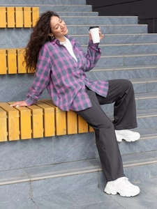Outdoor shot of a woman in a loose pink plaid shirt with grey trousers and white sneakers