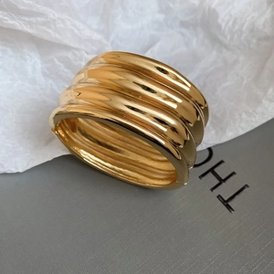 Detailed close-up of wide gold wavy cuff bracelet with high-polished mirror finish