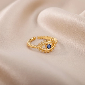Macro detail of gold-tone Evil Eye adjustable ring with blue stone on silk background