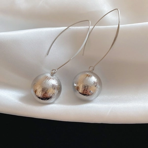 Close-up of silver brushed metal sphere earrings on white silk fabric background