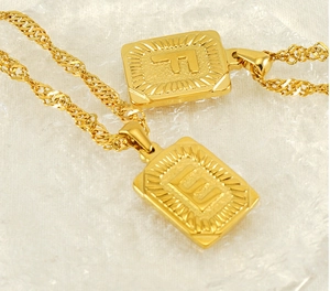Macro shot of gold stainless steel necklace featuring embossed letters F and E on square pendants