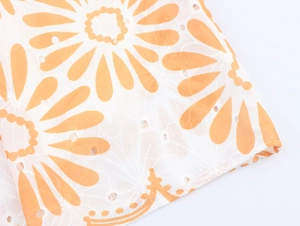 Détail de tissu blanc avec broderie florale orange et motifs ajourés en dentelle