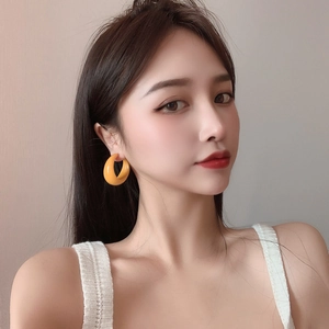 Close-up of bright orange C-shaped acrylic hoop earring on female model with soft lighting