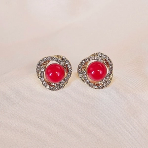 Macro detail of twisted gold earring with red pearl and rhinestones on silk