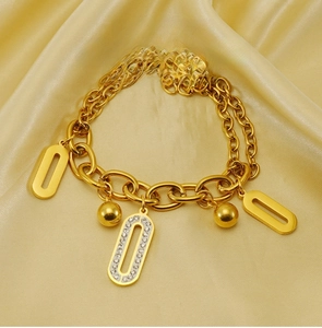 Détail du bracelet double couche en acier doré avec pendentifs ovales et zircons brillants