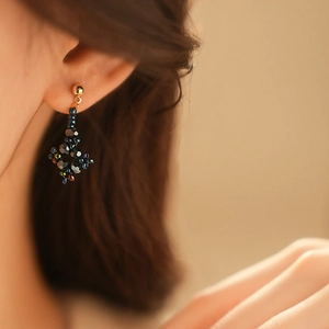 Detail of beaded floral diamond stud earrings in dark blue glass worn by model
