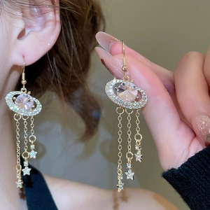 Macro detail of gold Saturn earring featuring pink gemstone, star ring and fringe tassels