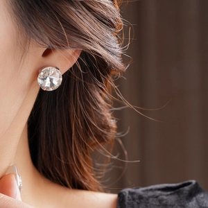 Close-up of a luxury silver earring featuring a large round crystal on a model's ear