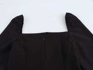 Detail van de vierkante halslijn en onzichtbare rits op deze zwarte geplooide jurk
