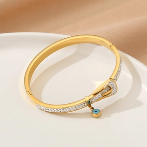 Vintage gold buckle bracelet with zircon stones and blue evil eye charm on white plate