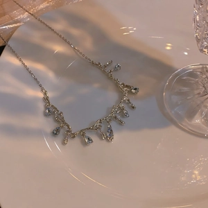 Elegant silver necklace with light blue teardrop stones and dainty tassels on white porcelain