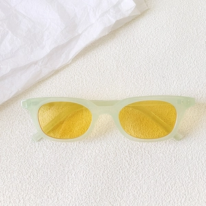 Detail view of mint green retro cat-eye sunglasses with vibrant yellow lenses on white texture