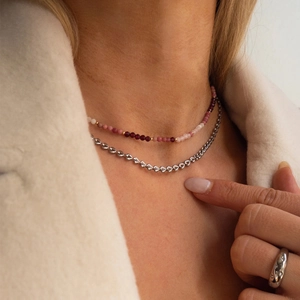 Detailed macro of layered 18k gold plated heart chain necklace and red beaded jewelry