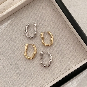 Close-up of irregular geometric gold and silver hoop earrings in a beige jewelry tray