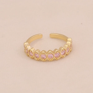 Gros plan d'une bague ouverte dorée ornée de zircons roses sur une surface beige
