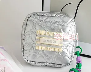 Détail d'une trousse de maquillage argentée à cœurs avec étiquette et poignée tressée